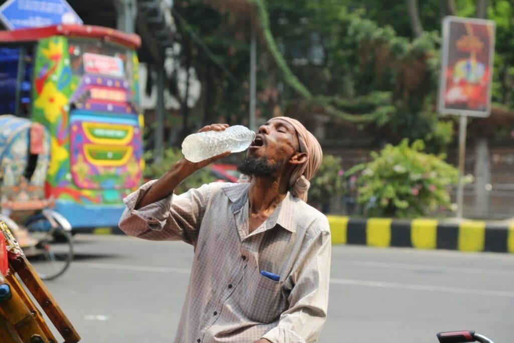 A rickshaw puller drinking water on a hot Dhaka street